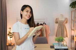 Happy asian woman entrepreneur standing and taking note in clothing store