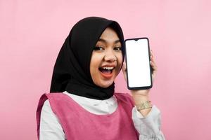 primer plano, de, hermoso, y, alegre, joven, mujer musulmana, tenencia, smartphone, con, blanco, o, blanco, pantalla, promoción, app, promoción, algo, aislado, publicidad, concepto foto