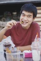 Hombre asiático comiendo un trozo de ternera a la parrilla con cara de felicidad foto
