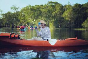 Mujer joven tomando fotos por teléfono móvil mientras navega en kayak de mar