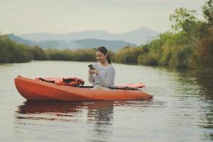 Mujer joven asiática leyendo el mensaje mientras navega en kayak en el río.
