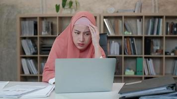 eine schöne muslimische Startup-Mitarbeiterin mit Hijab, die müde, gestresst und besorgt über das E-Commerce-Geschäft ist. das verliert durch Online-Internetbestellungen auf Laptops in kleinen Büros am Arbeitsplatz.