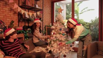 Family with dog and friends together are happily decorating the white Christmas tree in the home's living room, fun and cheerful prepare for a celebration party for the New Year festival holiday.