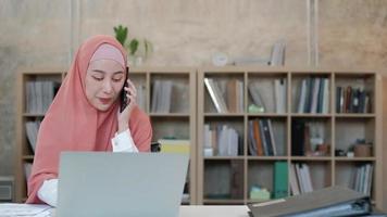 linda mulher de negócios islâmica está falando em sua comunicação de telefone móvel e sorrindo feliz porque pedido on-line de internet no laptop, estilo de vida moderno, ocupação de comércio eletrônico.