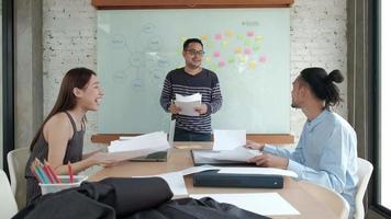 il team di ufficio professionale asiatico felice è allegro e celebra il successo degli affari dell'azienda. hanno gettato carte insieme, hanno volato in giro nella sala riunioni con foglietti adesivi colorati sulla lavagna.