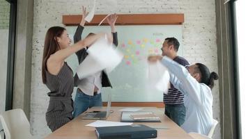 feliz equipo de oficina profesional asiático es alegre y celebra el éxito de los negocios de la empresa. arrojaron papeles juntos, volaron por la sala de reuniones con notas adhesivas de colores en la pizarra. video