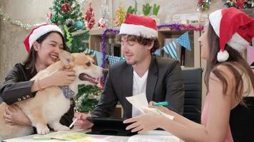 Equipo de tres trabajadores con sombreros rojos y perro, amigos y colegas hablando y relajante reunión en la oficina antes de las vacaciones de la empresa, decoración festiva para celebrar la fiesta de Navidad y el día de año nuevo. video