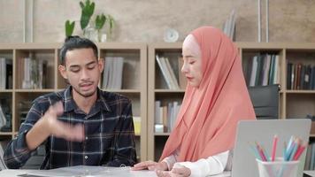 twee jonge startende collega's die islamitische mensen zijn, praten met een glimlach over succes in een e-commercebedrijf. gebruik laptop voor online communicatie via internet in een klein kantoor. video