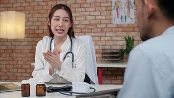 belle femme médecin en chemise blanche qui est une personne asiatique avec stéthoscope examine la santé d'un patient masculin dans une clinique médicale sur fond de mur de briques, souriant conseillant une profession de spécialiste médical. video