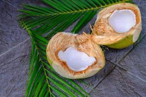 fruta de coco verde fresca cortada por la mitad y hojas de coco foto