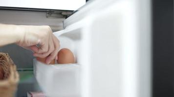 Female chefs hand place raw dairy organic chicken eggs from market in a chilled compartment of the refrigerator to keep fresh before cook as a breakfast meal, healthy protein foods but high calorie.