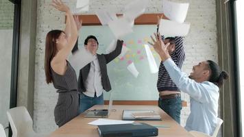 il team di ufficio professionale asiatico felice è allegro e celebra il successo degli affari dell'azienda. hanno gettato carte insieme, hanno volato in giro nella sala riunioni con foglietti adesivi colorati sulla lavagna. video
