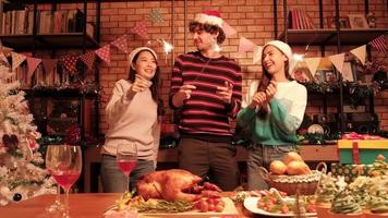 Grupo de tres jóvenes amigos bailando la felicidad y alegres fuegos artificiales de bengala, celebran el festival de Navidad en la mesa del comedor con regalos y alimentos, decorado en casa para la noche de la fiesta de año nuevo. video