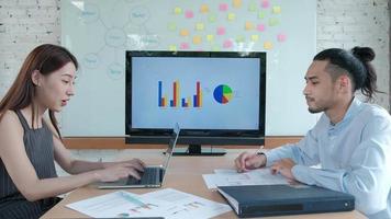 Female colleague presents business chart to male partner using a laptop in a meeting room, discussing the company's finances project. video