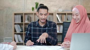 två unga startkollegor som är islamiska människor pratar om finansiella projekt med en kund med ett leende, presentationsframgång med ett affärskarta på skrivbordet på en liten kontorsarbetsplats. video
