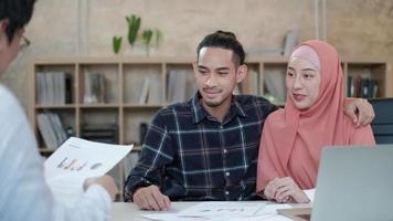 Zwei junge Startup-Kollegen, die islamische Menschen sind, sprechen mit einem lächelnden Kunden über Finanzprojekte, Präsentationserfolg mit einem Geschäftsdiagramm auf dem Schreibtisch eines kleinen Büroarbeitsplatzes. video