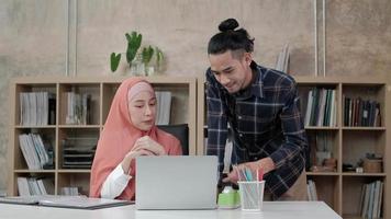 dois jovens colegas muçulmanos de startups falam com um sorriso sobre o sucesso de trabalhar em uma empresa de comércio eletrônico. use o laptop para comunicação on-line pela Internet em um pequeno escritório. video