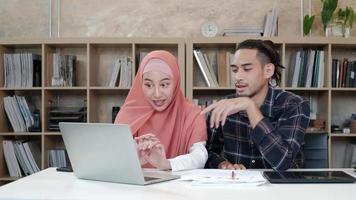dois jovens colegas de inicialização que são casais islâmicos falam com um sorriso sobre o sucesso de trabalhar em um negócio de comércio eletrônico. use o laptop para comunicação on-line pela Internet em um pequeno escritório. video