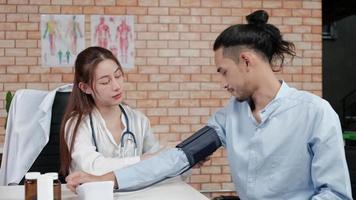 belle femme médecin en chemise blanche qui est une personne asiatique avec stéthoscope examine la santé d'un patient masculin dans une clinique médicale sur fond de mur de briques, souriant conseillant une profession de spécialiste médical. video