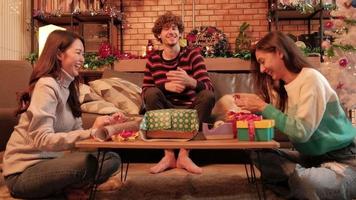la famille et les amis préparent ensemble des cadeaux avec une joie souriante et amusante pour la fête du réveillon de Noël dans le salon de la maison, joliment décoré pour des vacances de bonheur festif et la célébration du jour de l'an. video