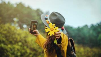 una niña con una mochila está usando el teléfono para tomarse una foto de la flor amarilla bua tong. girasol mexicano