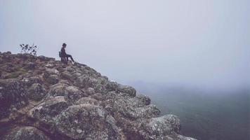 Asian women travel relax in the holiday.  Sitting on a rocky mountain cliff. Wild nature wood on the mountain. photo