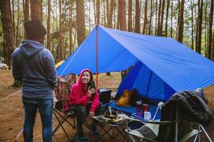 young asian couple of happy enjoying Camping in the pine forest Sit and eat food at the Camping page in the midst of nature. photo