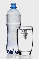 Resumen de salpicaduras de vidrio de botella transparente de agua azul con burbujas en blanco. foto