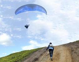 A young woman climbs up a mountain to meet a paraglider hovering in the air photo