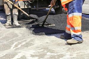 The working team evenly distributes hot asphalt with a shovel and wooden level manually over the repaired road section. photo