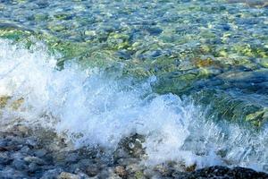 A splash of pure turquoise sea wave on pebble on the seashore.