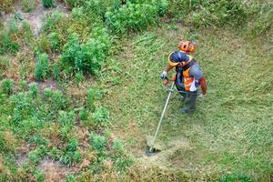 Worker mows tall grass with an industrial petrol trimmer, top view. photo