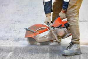 A construction worker cuts old asphalt with a portable petrol saw and a diamond cutting disc.