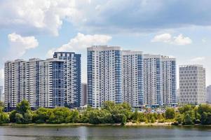 The facades of new residential high-rise buildings on the banks of the river and against the blue cloudy sky.