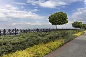 A cobbled stepped path along the embankment of the river, framed by a metal decorative fence cut off by bushes and trees in a beautiful park photo