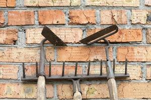 Garden tools old and rusty rakes and hoes against the old weathered brick wall photo