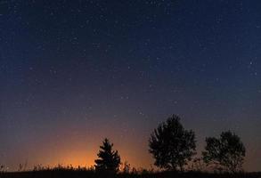 Silhouettes of three trees against the background of the night starry sky and the setting sun photo