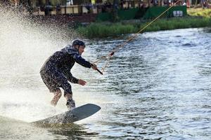 Wakeboarder corre a través del agua a alta velocidad a lo largo de las orillas cubiertas de hierba del río. foto