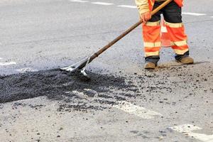 A road builder collects fresh asphalt on part of the road and levels it for repair in road construction. photo