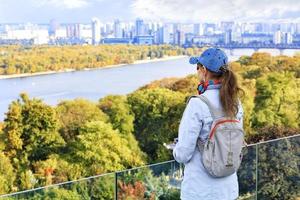 The traveler looks at the autumn cityscape of Kyiv with a view of the blue waters of the Dnipro River, Trukhanov Island and residential quarters of the left bank in blur.