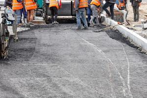 un grupo de trabajo de trabajadores de la carretera distribuye uniformemente la primera capa de asfalto caliente con palas manualmente sobre el tramo de la carretera que se está reparando. foto