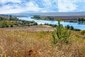 A beautiful summer landscape with a winding river between fields and hills and a blue, slightly cloudy sky. photo