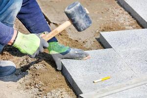 A worker lays down granite blocks on the sidewalk with a rubber hammer. photo