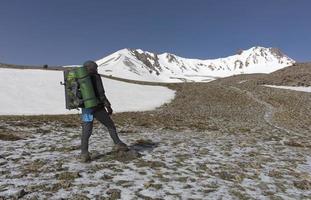 The tourist rises up the mountainside to the snow-capped summit photo