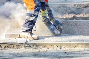 A worker cuts paving slabs on the road using an electric angle grinder and diamond cutting disc. photo
