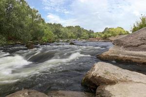 The river Southern Bug in the summer - rocky shores, rapids, fast river flow, bright green vegetation and a cloudy blue sky photo