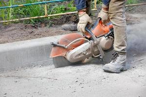 The road worker, using a petrol saw, cuts old asphalt. photo
