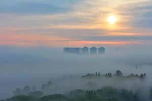 Foggy early morning in a spring city park against the backdrop of residential skyscrapers and the soft sun. photo