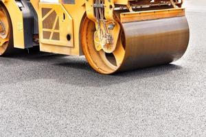 The massive metal cylinder of the road roller compacts the fresh asphalt on the construction site. Close-up. photo