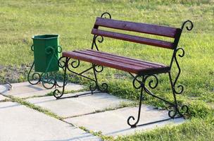 An old wooden bench stands on the lawn in the park and is painted with a brownish-red paint photo